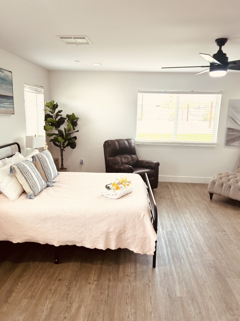 Spacious resident bedroom with blush bedding, art, ceiling fan, and large windows
