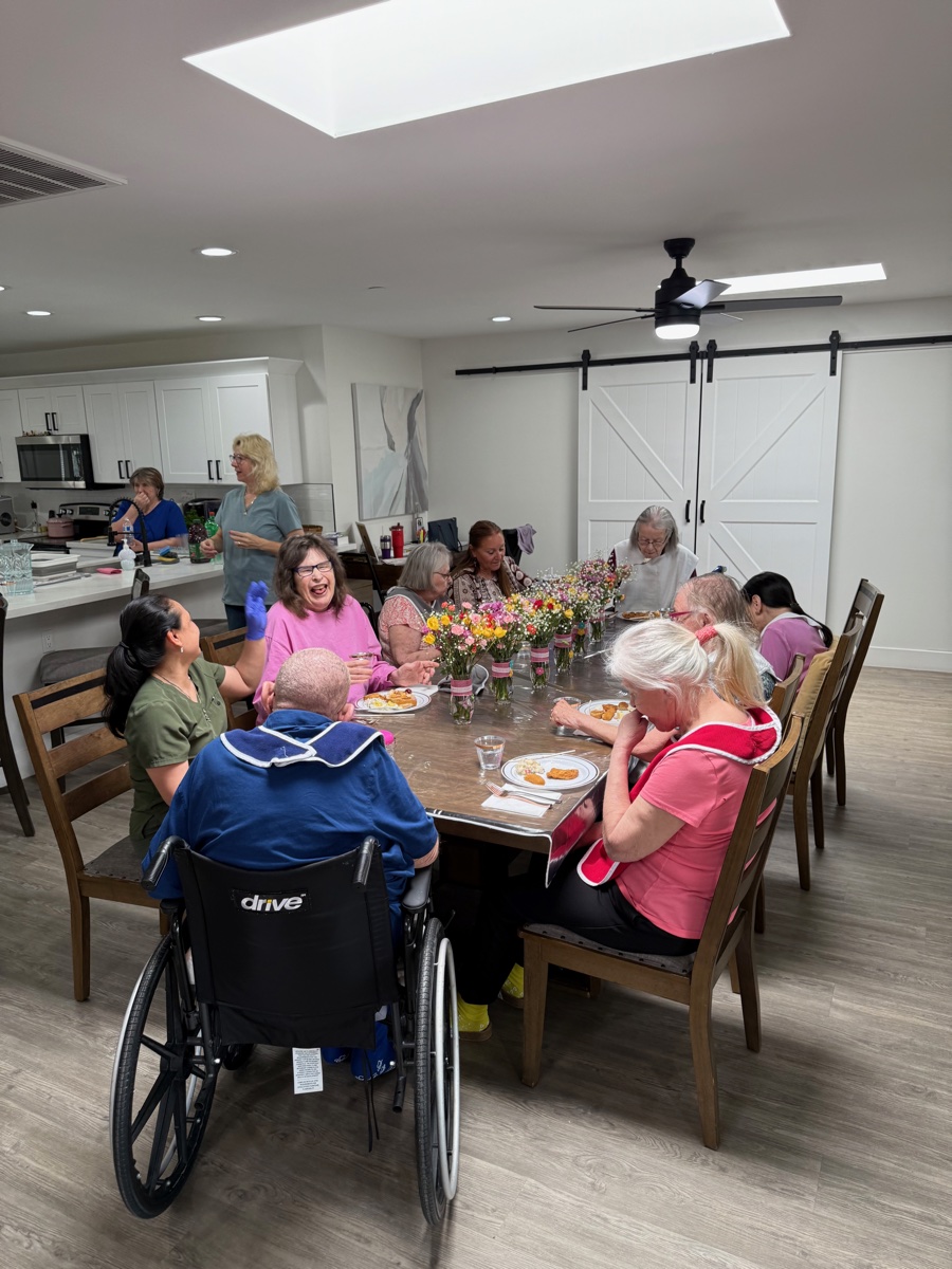 Residents and staff gathered around a dining table with bouquets of fresh flowers as centerpieces