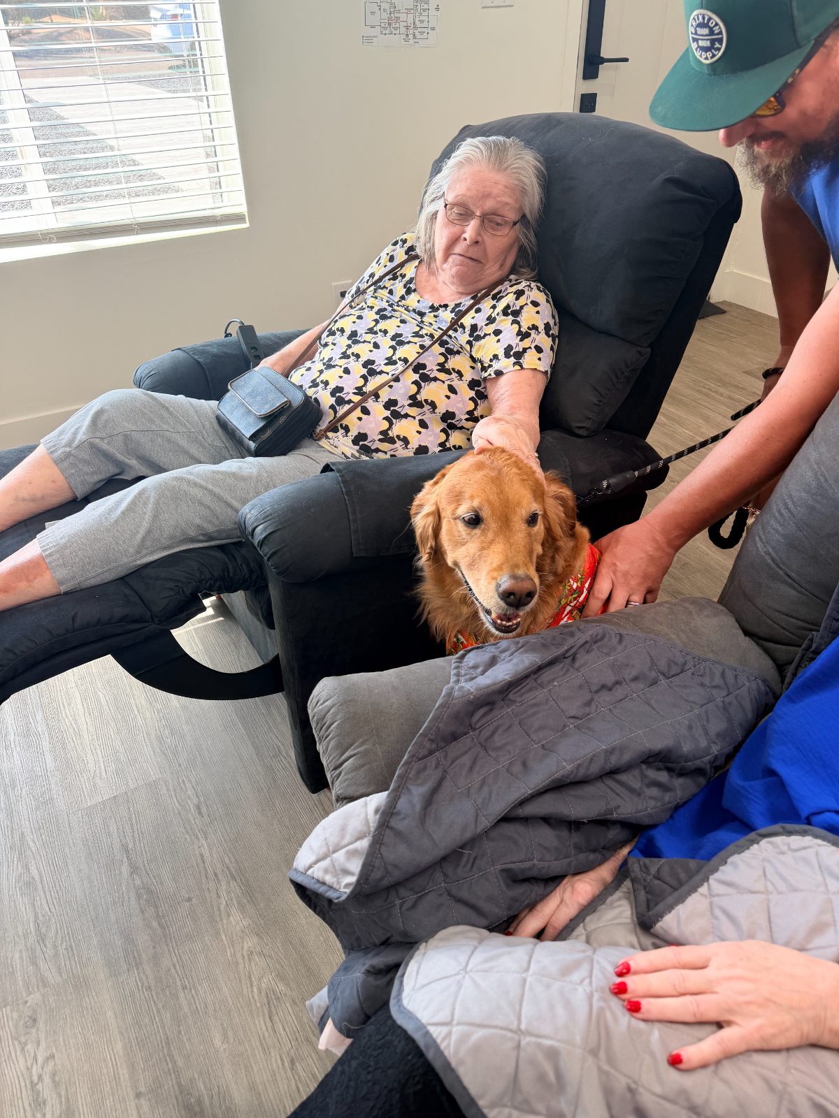 A resident in a recliner rests her hand on Maui's head as he leans in beside her chair