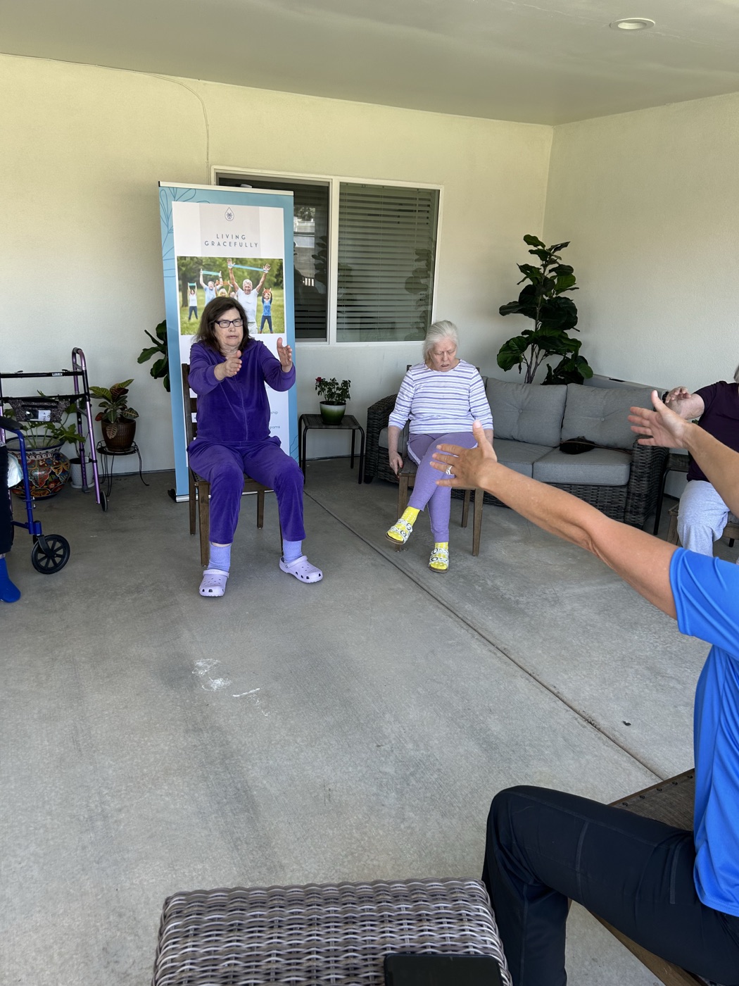 A resident extends her arms during a seated physical therapy session beside the Living Gracefully banner